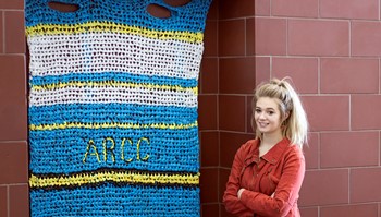 Anoka-Ramsey Community College President of the Student Sustainability Club, Paige Hanson (shown) stands by a mat the club produced for the organization Weaving for Love, which makes sleeping mats for the homeless. Collecting plastic bags for the mats is just one of the many activities the club does to promote environmental sustainability.