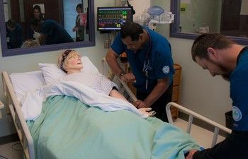 Nursing students checking vitals on practice dummy.