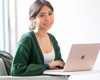 student in green sweater at laptop on campus