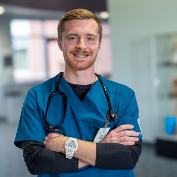 Medical professional in blue scrubs with stethoscope standing confidently in a clinic lobby.