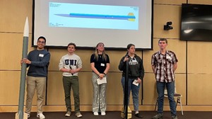 Five students stand in front of a presentation screen displaying the word