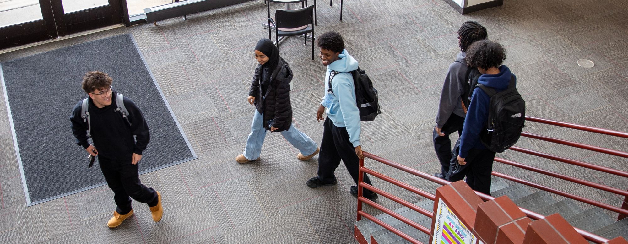 Coon Rapids Campus hallway five student walking down main staircase to lower level smiling
