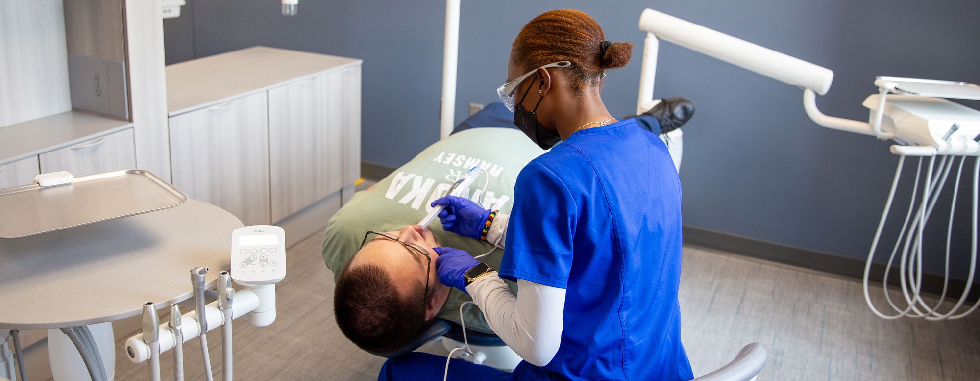 Dental assisting student performing a patient examination in a dental clinic training lab.
