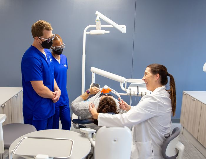 Dental assisting students observe an instructor working with a patient in a dental lab.