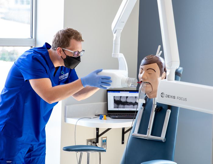 Student using dental X-ray equipment on a training mannequin.