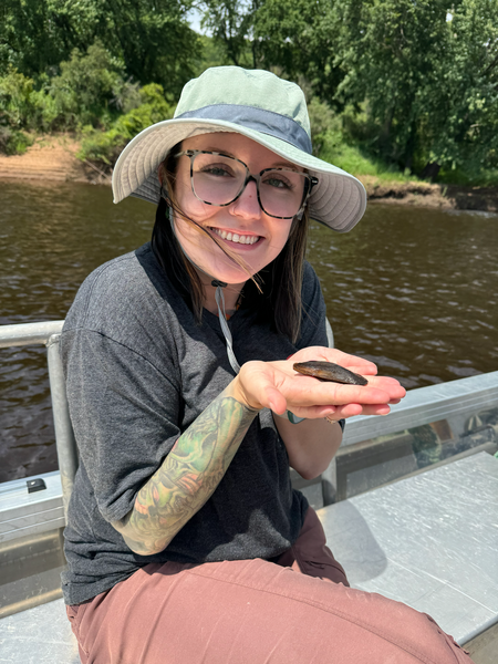 Individual holding marine animal in hands, smiling in outdoor environment.