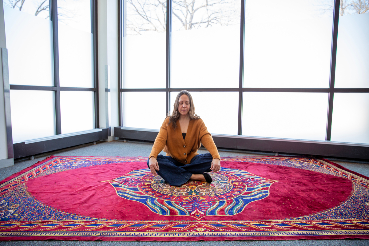 Individual seated cross-legged on vibrantly-colored rug.