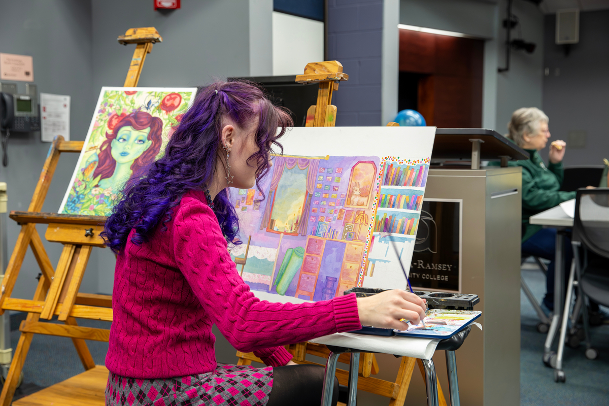 Individual in vibrantly-colored clothing painting in auditorium environment.
