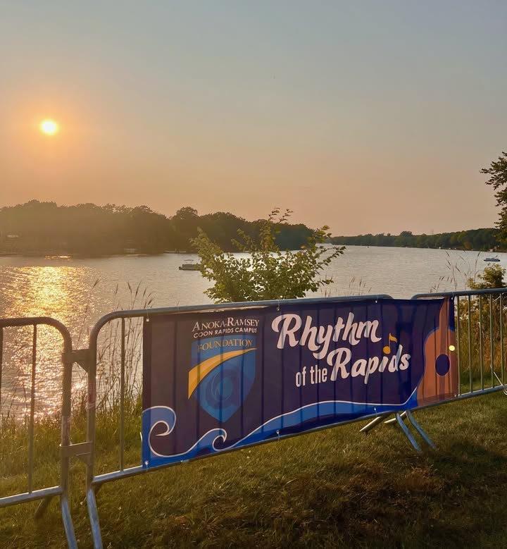 A banner with the Rhythm of the Rapids logo against a background of the Mississippi River at sunset