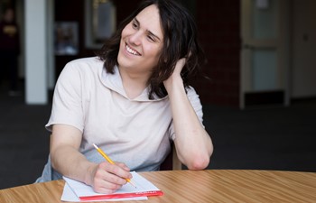 Student smiling at table with pencil and paper.