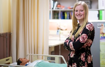 Student standing with arms crossed in medical room.