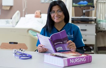 Student in scrubs reading a nursing textbook.