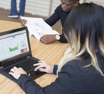 A student using a laptop, and another reading a book at a table