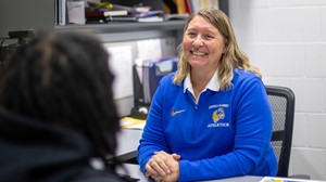 Athletic Director Jessica Pelzel sitting at desk, smiling while interacting with student