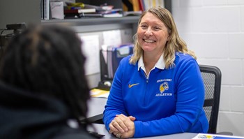Athletic Director Jessica Pelzel sitting at desk, smiling while interacting with student