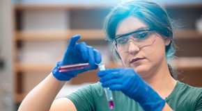student wearing gloves and goggles in lab pouring test tubes