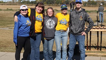 Five individuals standing in sunny setting, smiling at camera