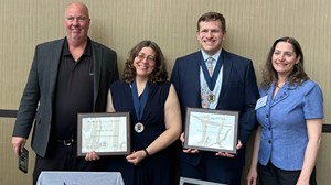 Four individuals standing near table, two holding awards. 